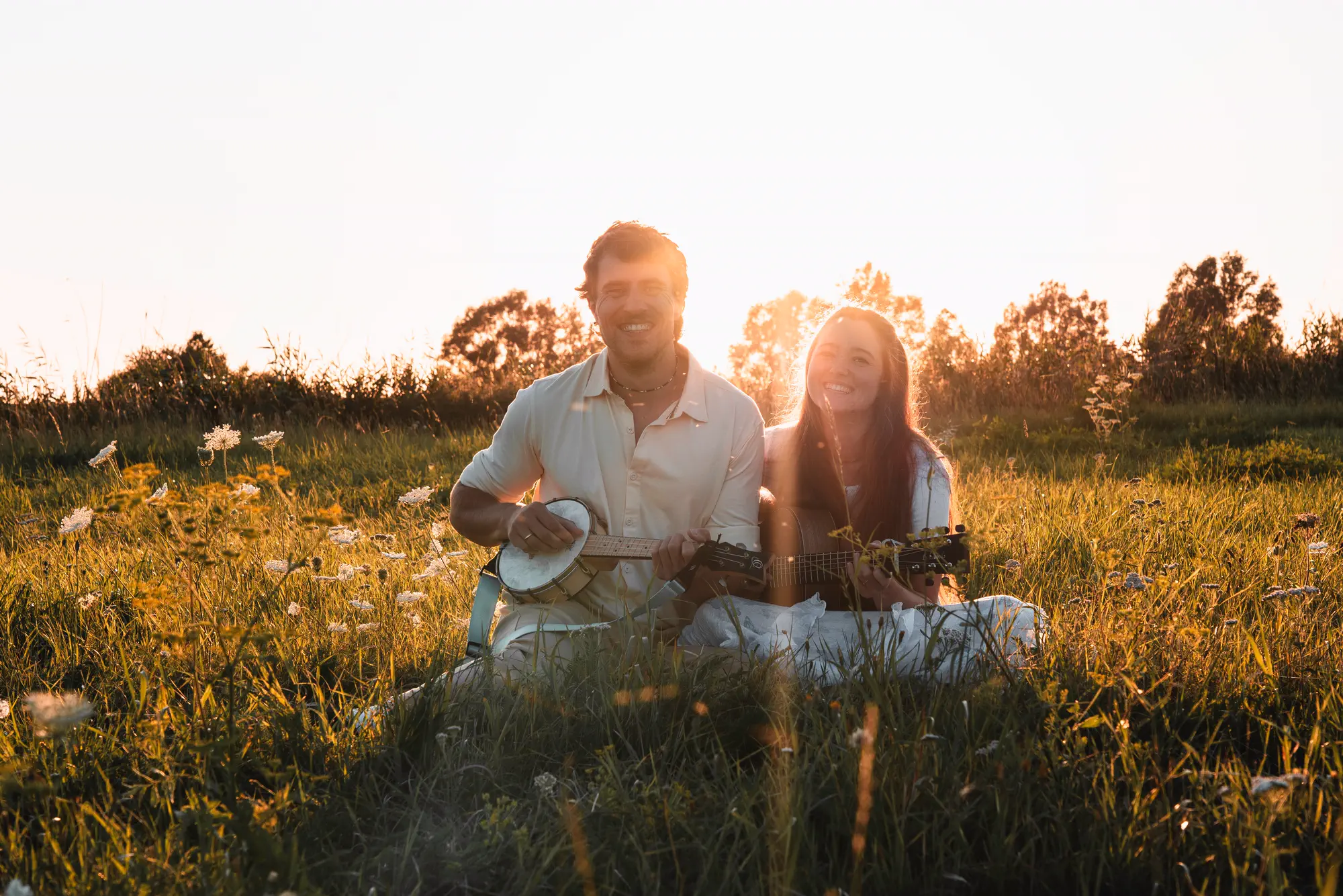 Sunny und Marty sitzen im Abendlicht in einer blühenden Wiese, er mit Banjo-Ukulele, sie mit Gitarre