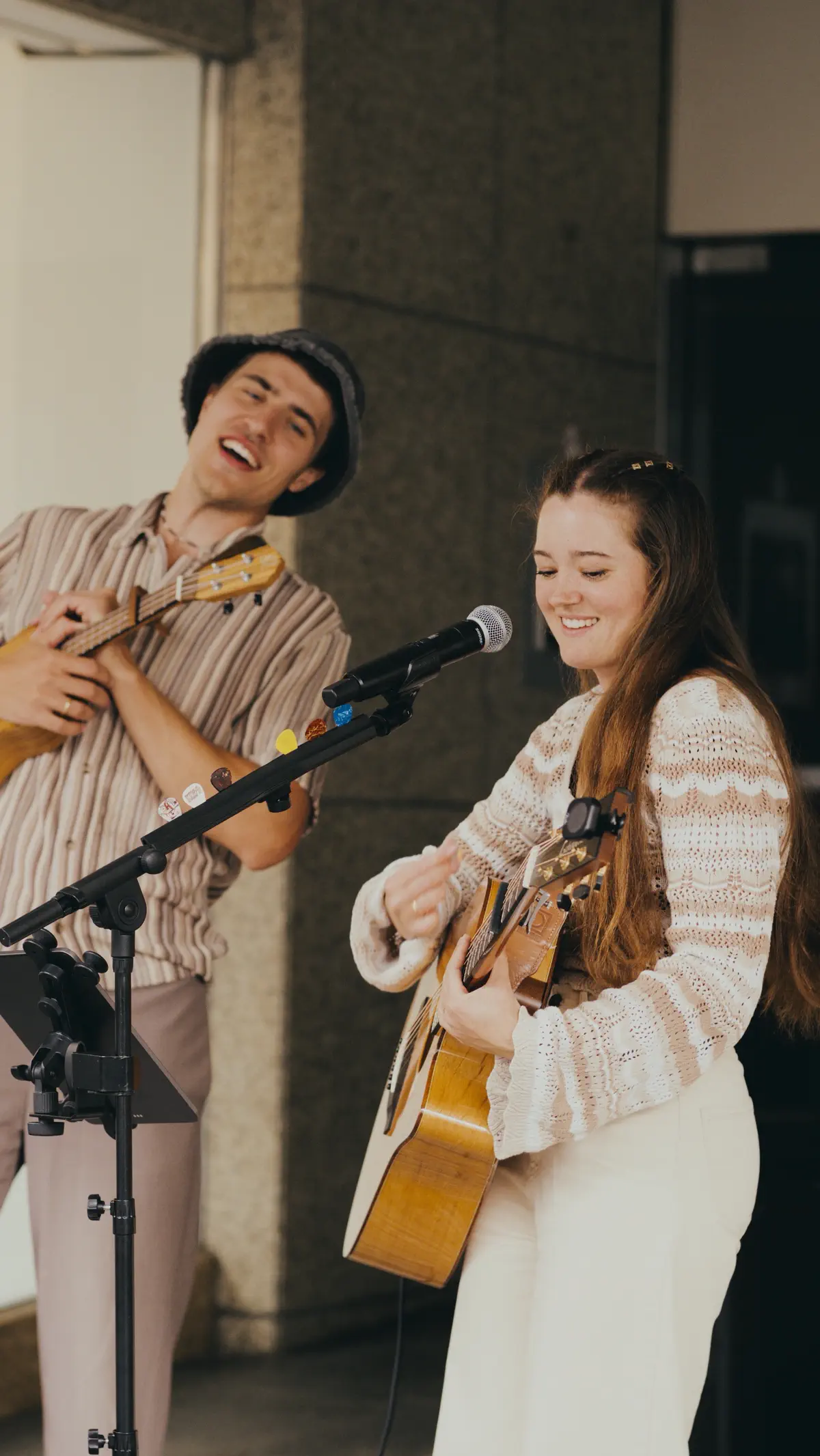 Sunny und Marty spielen live vor einer Steinfassade, er singt mit Ukulele, sie spielt Gitarre am Mikrofon